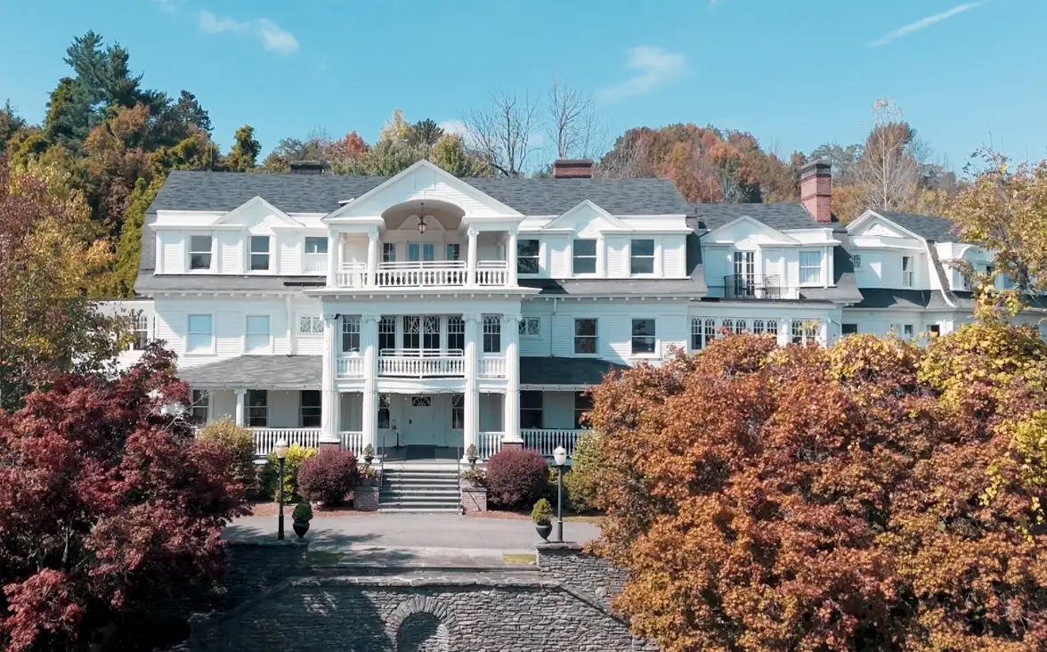 Front view of an elegant, large white mansion surrounded by colorful autumn foliage.