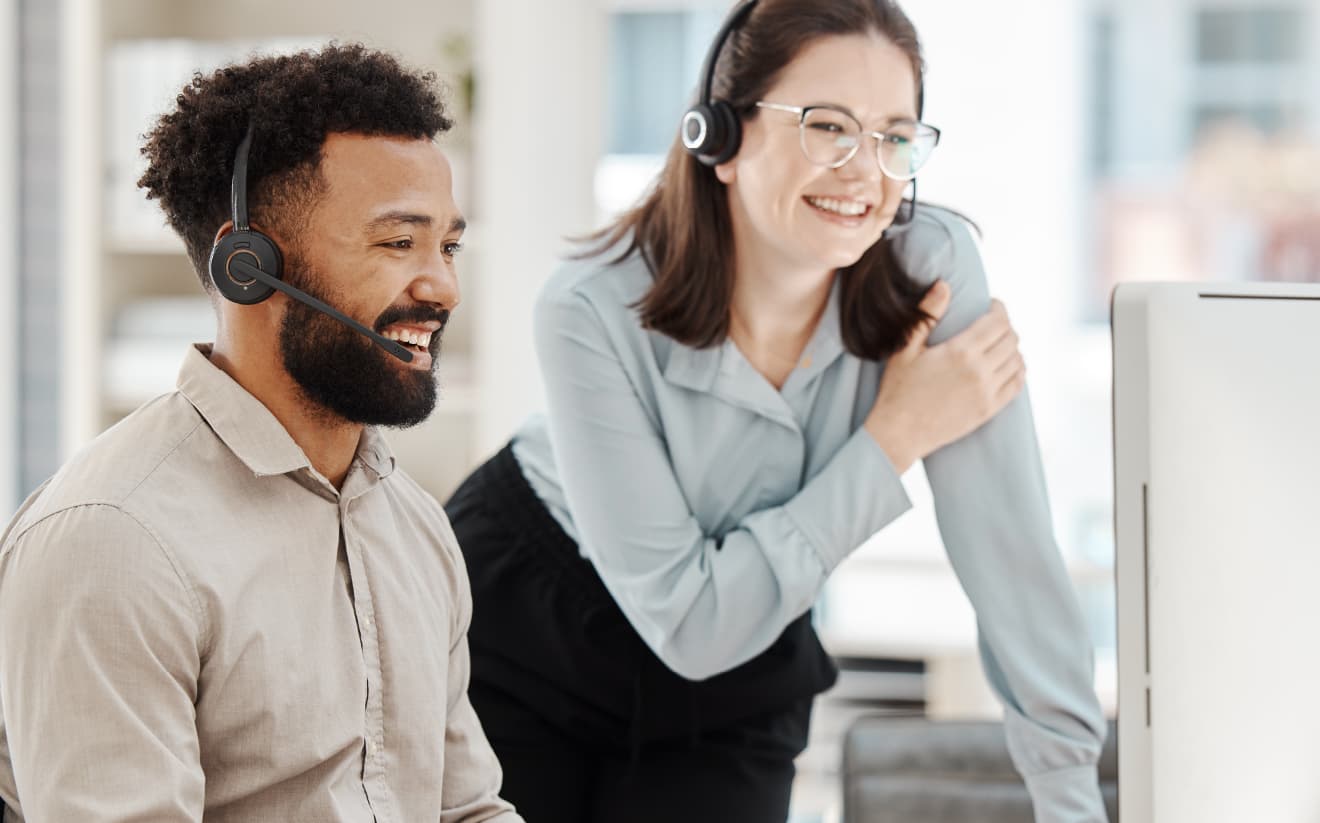 Two professionals working together at a desk, with one providing support and training, representing the role of an Account Manager to help configure accounts and train staff for success.