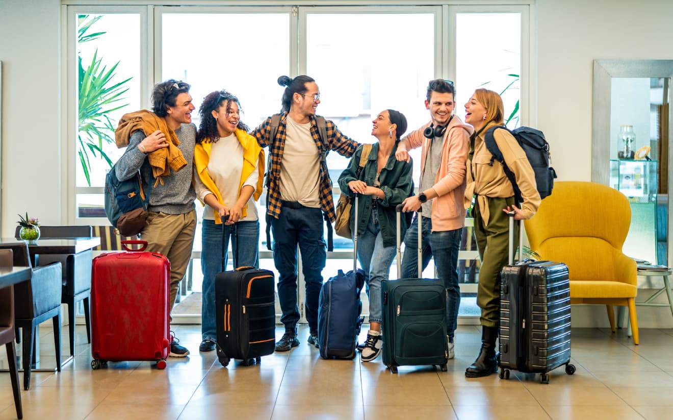 A group of six people standing together with luggage, representing the management of group reservations and the process of coordinating large room blocks and transferring charges across multiple folios.