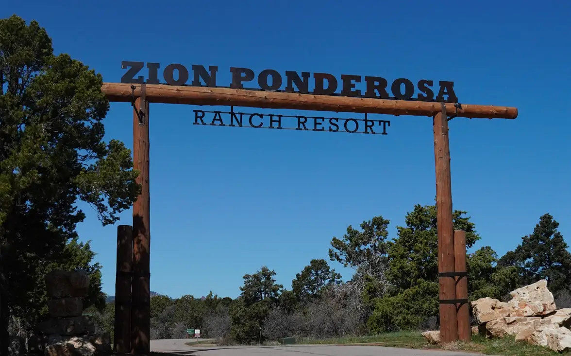 Entrance sign to Zion Ponderosa Ranch Resort, framed by trees under a clear blue sky.