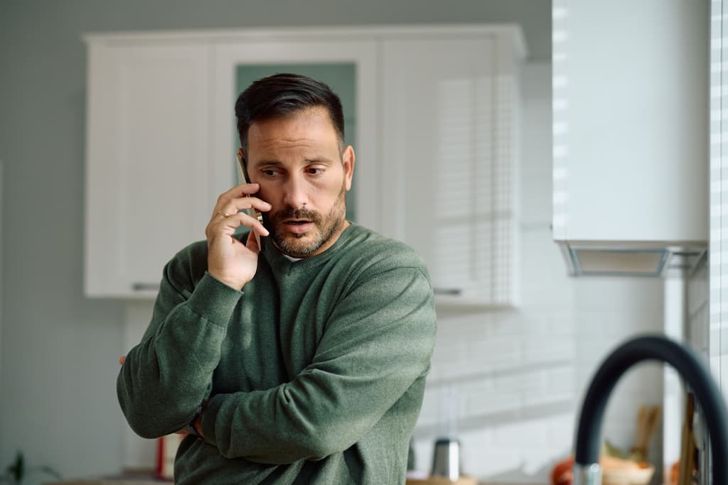 Distraught man receiving bad news while talking on cell phone at home