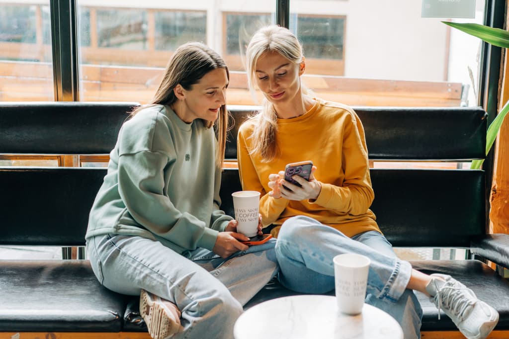 Two female friends looking at a phone screen while having coffee.