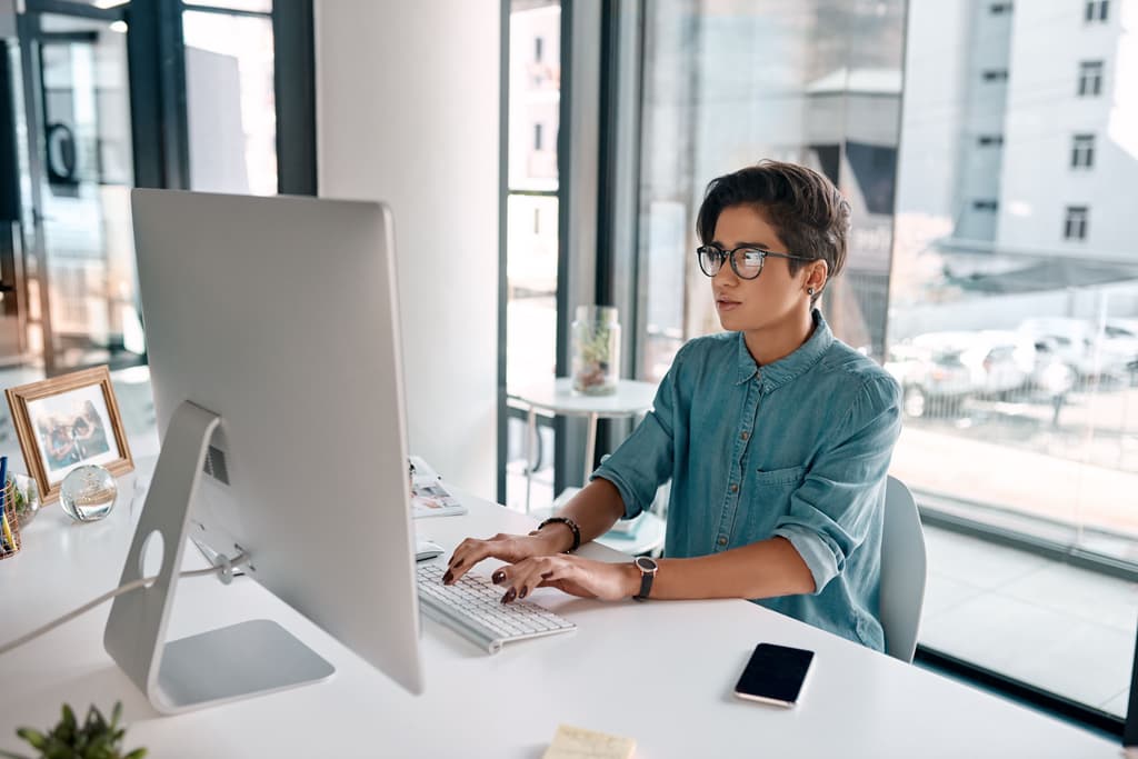 A person wearing glasses and a blue shirt working in front of computer