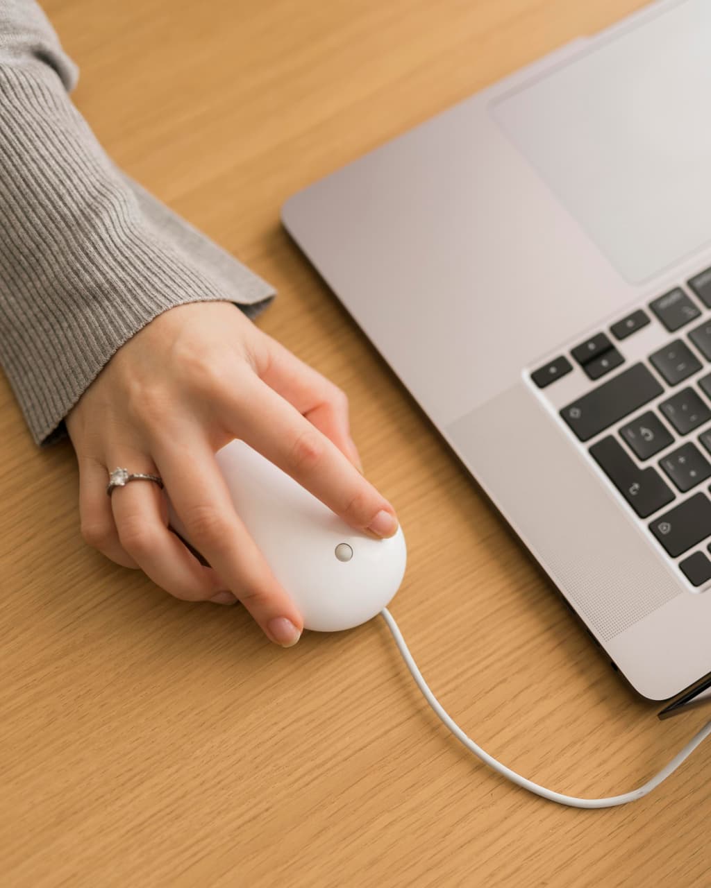A female user clicks on a white mouse with a cable connected to a computer