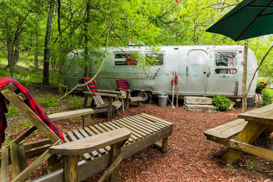 Airstream style trailer with outdoor furniture in a wooded setting