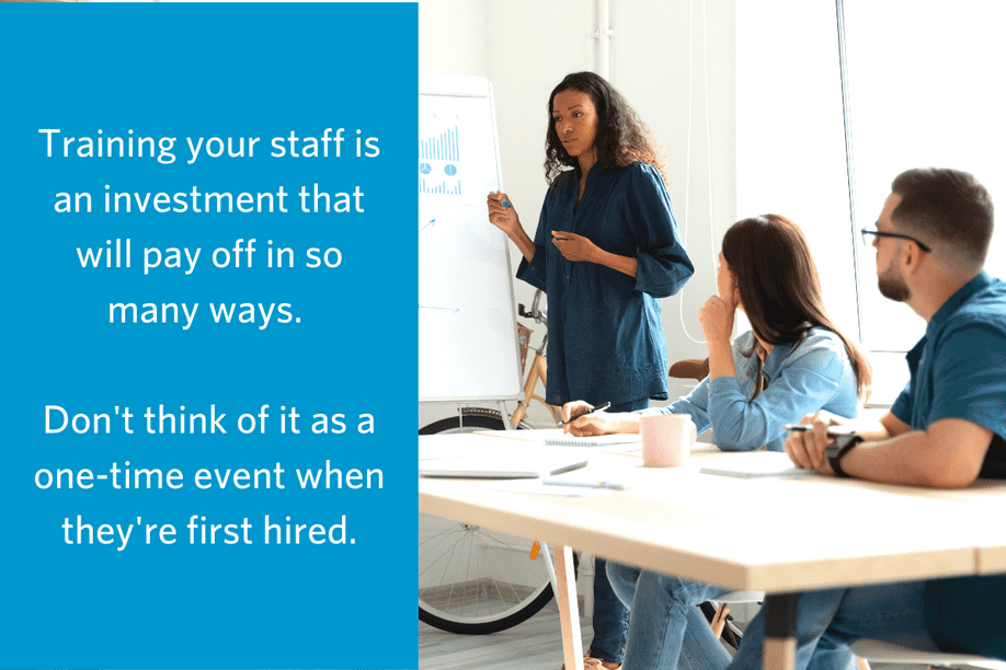 woman standing at a white board appearing to be addressing a table of other people with text reading Training your staff is an investment that will pay off in so many ways. Don't think of it as a one-time event when they're first hired.